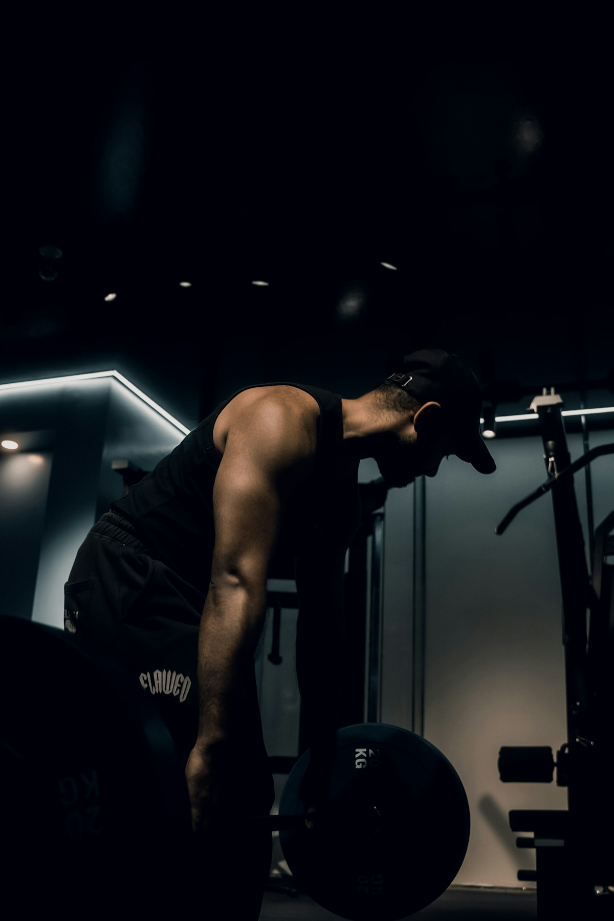 Idrottare lyfter en skivstång i ett mörkt gym med sidoljus