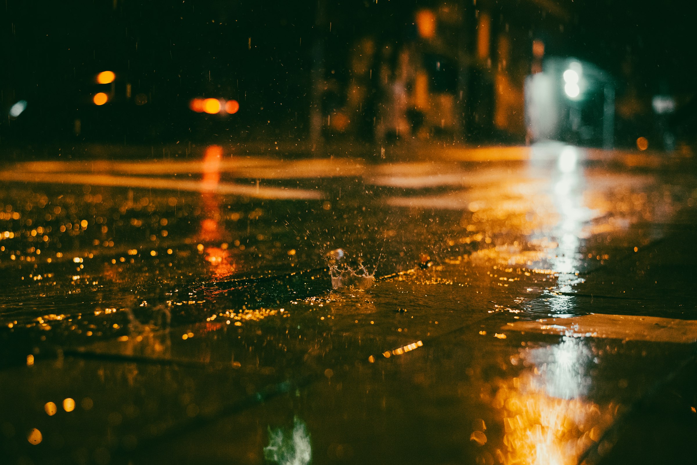 Regn som slår ner i blöt asfalt under gatljus mitt i natten